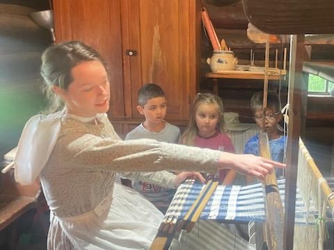 Woman demonstrating how to use a loom.