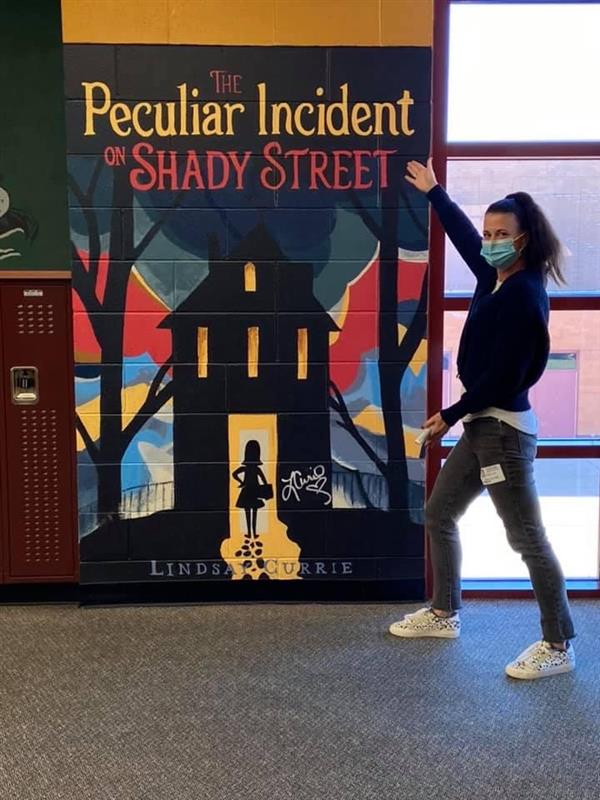 Author Lindsay Currie poses with the mural of her book cover.