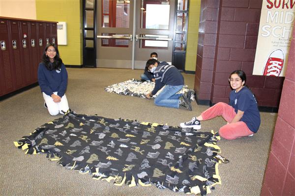 2 students sit on the ground next to a blanket that they made