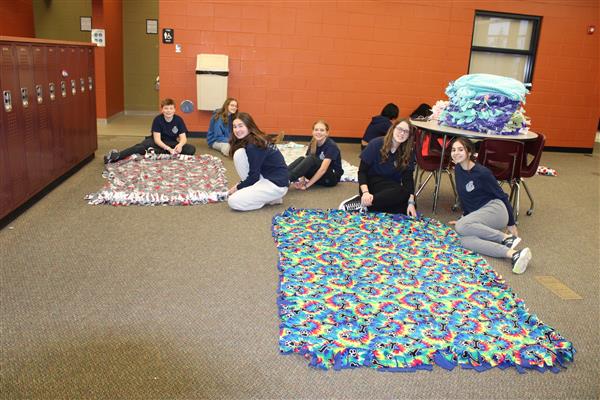Several students sit next to a blanket they made