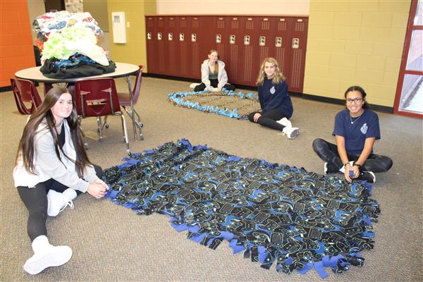 Several students sit on the ground next to a blanket that they made