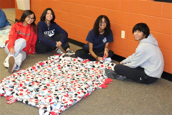 3 students sit next to a blanket that they made