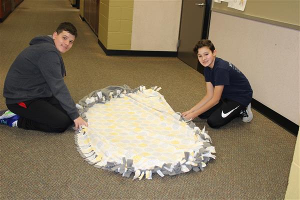 2 students sit on the ground next to a blanket that they made