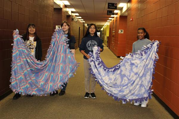 Several students hold up blankets that they made in a service project