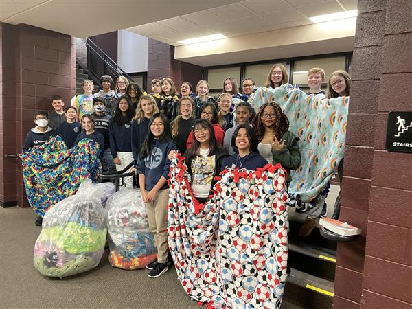 Students pose in a group holding the blankets that they made