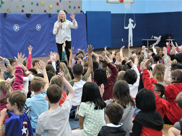 author asking students a quesiton and students have hands up sitting in front of her
